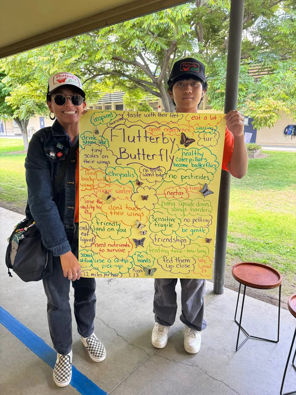 Students holding a hand-drawn 'FlutterBy Butterfly' learning poster
